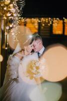 A bride and groom are standing in front of a building with lights photo