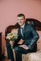 A man in a suit and tie is sitting on a bed with a bouquet of flowers in his lap photo