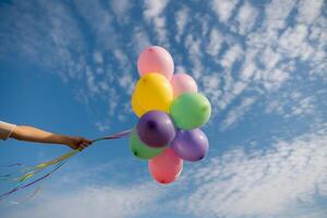Arm holds colorful balloons against clear blue sky with scattered clouds photo