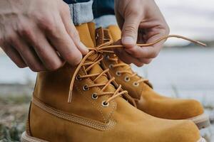 Yellow boots being laced beside a backdrop of sky and water photo