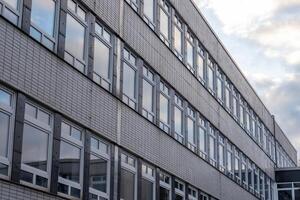 Modern building exterior showing multiple rows of windows reflecting cloudy sky photo