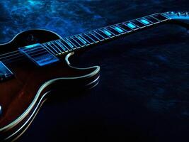 Electric guitar resting on a dark surface with blue backlight photo