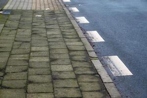 Damaged sidewalk tiles by the road with white lines photo