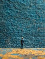 Miniature man in suit standing in front of blue wall photo