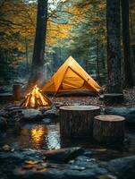 A serene camping scene with a yellow tent, campfire, and tranquil stream in a forest. photo