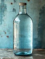 A clear glass bottle with a cork stopper, resting on a textured surface against a blue background. photo