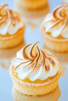 Mini lemon tart with golden crust and silky lemon curd topped with toasted meringue reflecting on a glossy surface photo