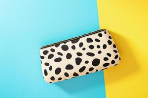 Leopard-print clutch bag with sleek black leather details on textured surface illuminated by bold studio lighting photo