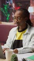Vertical Student at home drinking coffee and browsing internet on notebook, researching information online. Woman enjoying hot beverage while reading internet articles on laptop for school tasks, camera A video