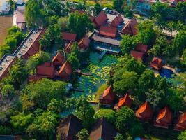 Aerial view of red roofed Thai buildings with pointed gables, surrounded by lush greenery and a large lotus pond filled with lily pads in Phuket, Thailand. photo
