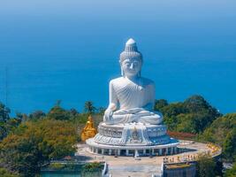 The iconic white marble Big Buddha statue in Phuket, Thailand, stands on a hilltop with ocean views, surrounded by greenery and a paved platform. photo