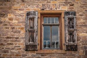 Rustic wooden window framed by aged stone wall reflects calm sky in a quaint rural setting photo