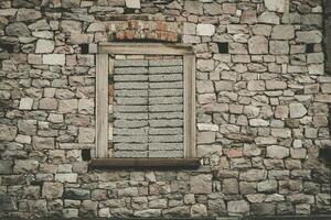 Stone wall with boarded window showcasing aged textures and rustic charm in an abandoned setting photo