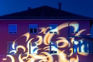 Colorful light patterns dance across a building facade in an evening display of artistic projection photo