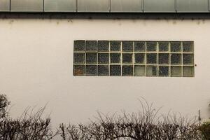 Glass block window adorned with fading graffiti on a plain wall in an urban setting during daylight photo