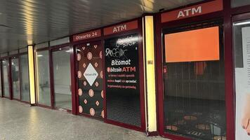 Warsaw, Poland. November 01, 2024. A Bitcoin ATM machine located in a public space, in a underground passageway. The machine has a red and black design with a prominent Bitcoin photo