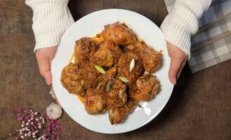 Close-up of a plate of delicious looking chicken drumsticks in a rich sauce, garnished with green onions and garlic photo