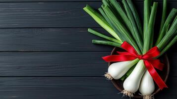 Fresh green onions tied with red ribbon on dark wooden surface with copy space. Greeting card for St. Davids day. photo