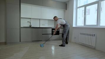 A builder in uniform washes the floor in a new apartment. The concept of construction and repair. video