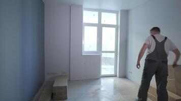 ein Baumeister im ein Arbeit Overalls bewegt Kisten und bereitet vor zu montieren Möbel im ein Neu Wohnung. Montage Möbel im ein Neu Wohnung. video