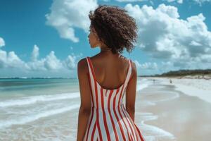Woman in a striped dress stands by the beach with dark clouds overhead photo