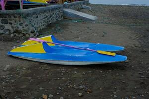 A blue and yellow paddle boat rests on the beach with two pink paddles photo