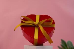A heart shaped red box with a gold ribbon sitting on a surface photo