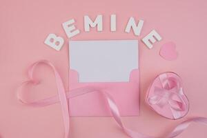 A pink envelope containing a blank card surrounded by a pink ribbon forming a heart a heart shaped gift box with a pink ribbon and the words Be Mine spelled out in white letters photo