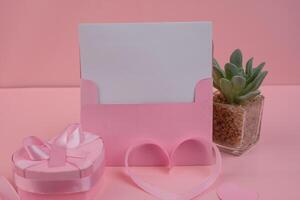 A pink card stands with a heart shaped ribbon and a heart shaped gift box. invitation mockup photo
