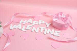 Happy Valentine message spelled out with white letters surrounded by pink hearts and ribbon next to a heart shaped gift box with a pink ribbon photo