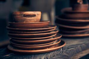 A stack of clay plates of different sizes on a dark background. Level position, top view. Brown plates are on a wooden shelf photo