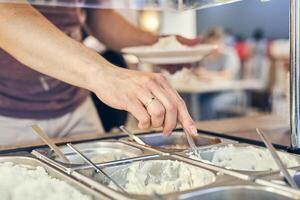 Self-service canteen in the office center. A man's hand dials white sauce into a plate. A variety of sauces on a metal tray with space for copying photo
