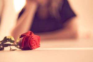 Close up of beautiful red rose on a narrow beam of sunlight on the background of a blurry image of a woman. Backdrop with copy space, empty, peach fuzz. Template, mock up for your design, text, card photo