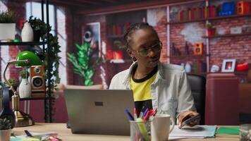 Upset woman receiving bad news from text message on smartphone while using notebook in home office. Sad remote worker troubled by SMS received on mobile phone while using laptop, camera B video