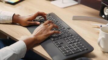 Person at home office desk typing on PC keyboard next to coffee mug, close up shot. Remote employee in apartment pressing computer peripheral keys, inputting data, camera B video