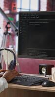 Vertical Developer at computer desk coding while listening music, creating software, implementing algorithms. Remote worker with headphones on at home working with code editor, building applications, camera B video