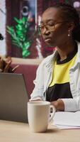 Vertical Woman in home office sitting at desk in front of laptop, answering phone call. Remote employee using notebook to do job online, receiving telephone call on smartphone, camera A video