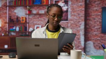 Woman at home taking break from work to look at social media feed on tablet. Remote employee at work in apartment office pausing tasks to use social network application on device, camera B video