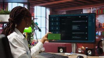 Woman seated at desk using isolated screen mobile phone to follow tutorial on AI LLM chatbot software. African american person uses mockup smartphone in apartment and GPT program on computer, camera A video