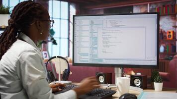 Engineer in home office looks at UI on computer monitor, typing and executing programming code. Panning shot of IT worker using coding application to write and test code in modern apartment, camera A video