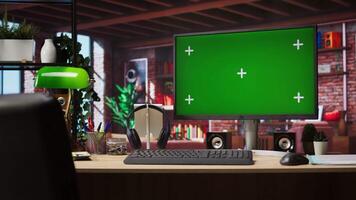 Green screen mockup desktop PC display on cozy home office desk with audio devices. Chroma key computer monitor in colorful modern loft with brick walls and plants on shelves video