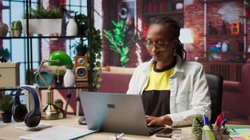 Portrait of cheerful woman in home office opening laptop, starting working on tasks. Joyous african american person using electronic notebook device to do job online, camera A video