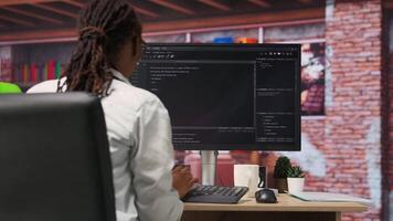 Programmer types code into PC, entering commands, running script. African american IT professional in apartment fixing errors in application, implementing new features, camera B video