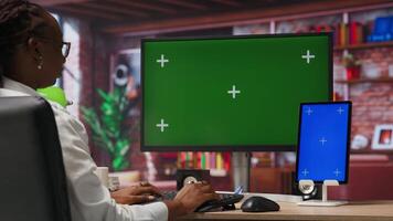 Remote employee in home office using green screen PC and mockup tablet to work on job tasks. Teleworker using chroma key computer monitor and isolated screen device to do job online, camera B video