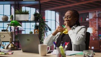 Teleworker in home office stretching back and yawning, feeling fatigued while working on laptop. Jaded african american remote employee relaxing muscles, solving tasks on notebook, camera A video