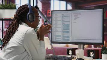 Jolly engineer in home office working on computer, dancing at desk in celebration after successfully executing code. IT worker wearing headphones happy after finishing compiling code, camera B video