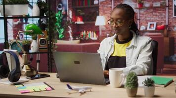 Remote worker at home office desk drinking coffee and browsing internet on notebook, researching information. Woman enjoying hot beverage while using search engines to find data for work, camera A video