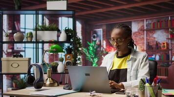 Portrait of smiling student at home browsing internet on notebook, doing homework, researching information online. Cheerful girl in apartment reading articles on laptop for school tasks, camera A video