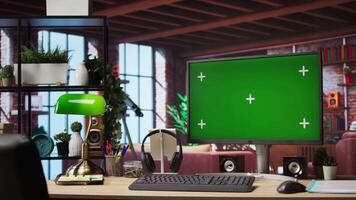 Isolated screen mockup PC on home office desk with stationary items and headphones on, surrounded by plants. Chroma key computer display in loft with shelves filled with books in background video