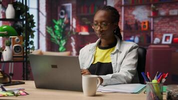 Woman in home office stretches back, feeling fatigued while working on laptop. Remote employee in apartment feeling backpain, relieving pain, solving tasks on notebook, camera B video